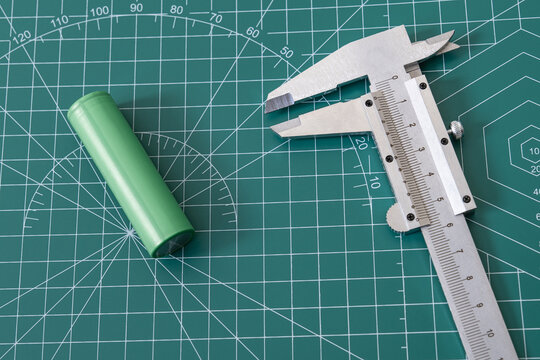 caliper and 18650 lithium-ion battery on a green cutting mat. oncepts of precision engineering, electronics prototyping, standardized battery sizes, and technical measurement in hardware development.