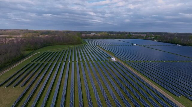 Aerial view of a large solar farm with rows of blue solar panels surrounded by green trees under a cloudy sky Indianapolis, Indiana, United States.