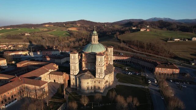 Aerial view of Santuario di Vicoforte with its massive elliptical dome and four bell towers surrounded by historic buildings and rolling hills in Vicoforte, Piedmont, Italy.