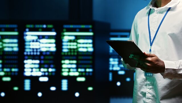 IT specialist walking through server rows performing data backups, close up. Serviceman using tablet to make sure electric generators are able to ensure operational continuity