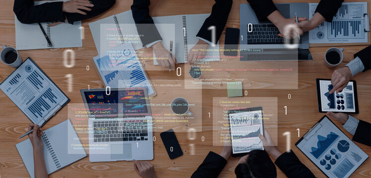 A business team collaborates in a modern workspace, analyzing data on laptops and tablets with documents spread out, reflecting productivity and strategic planning. Trope