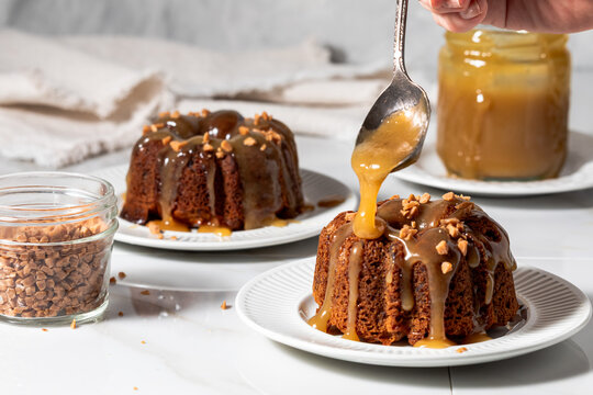 Caramel sauce being spooned onto freshly baked sticky toffee pudding cakes.