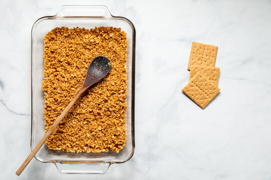 A glass baking dish with crushed graham crackers to make a dessert base layer.