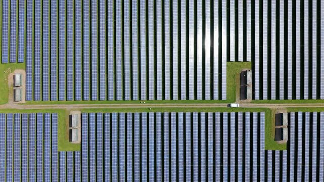 Aerial view of the Tutbury solar energy farm with rows of solar panels and a white van on a path in Tutbury, England, United Kingdom.