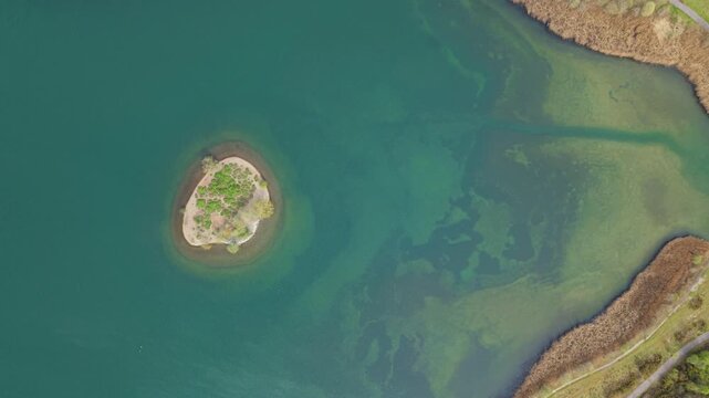 Aerial view of Albert Village Lake featuring a small circular island surrounded by turquoise water and shoreline reeds in Swadlincote, England, United Kingdom.