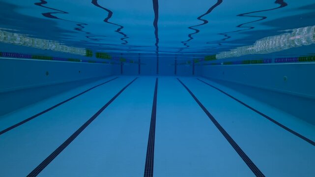 Underwater shot of an empty indoor swimming pool with blue tiles and clear water.