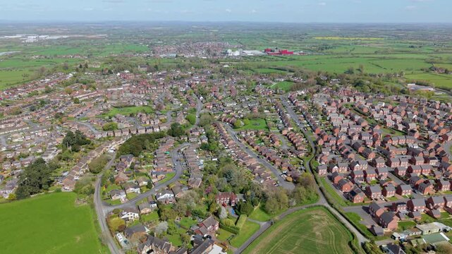 Aerial view of residential houses and lush green fields under a clear blue sky in Tutbury, England, United Kingdom.