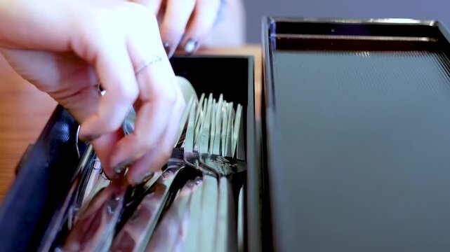 Close up of hands sorting through shiny metal cutlery in a black organizer box.