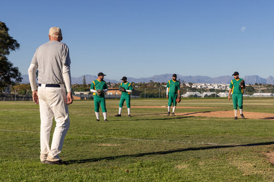 Mature male coach standing and coaching players on grass baseball field with gloves, copy space