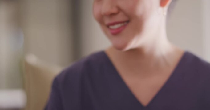 Asian woman in scrubs rotating pill bottle, reading label, explaining dose in clinic, watch visible