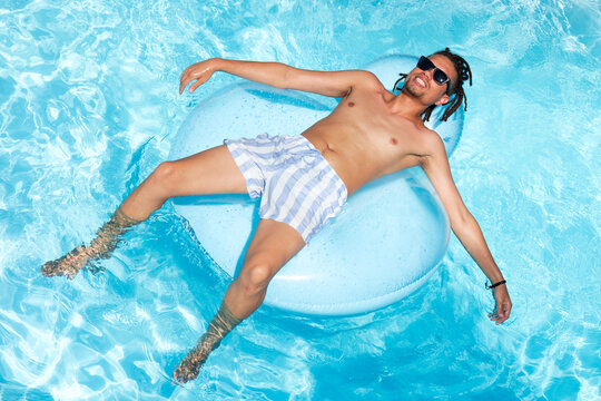 African American man floating on inflatable ring in clear pool, wearing striped trunks and shades