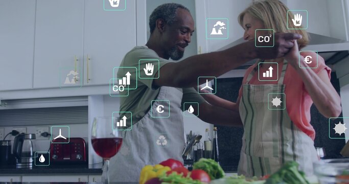 Dancing couple in aprons preparing food in home kitchen, with vegetables, wine glass, overlay icons