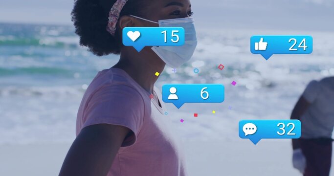 Gazing woman wearing surgical mask pink tee patterned headband at beach showing blue notifications