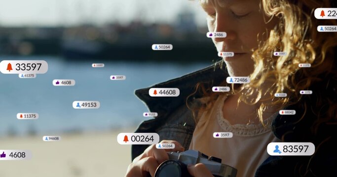 Holding compact camera, blond woman in jacket checking controls at shore, badges, copy space