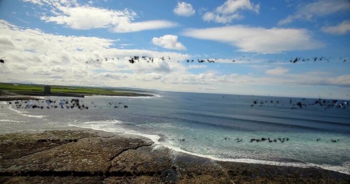 Showing rocky shore, breaking surf and open sea at coast, with square tower, grass, lens smudges