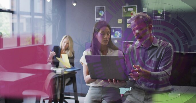 Collaborating co-workers sharing laptop in office, in white blouse and blue shirt, yellow folder