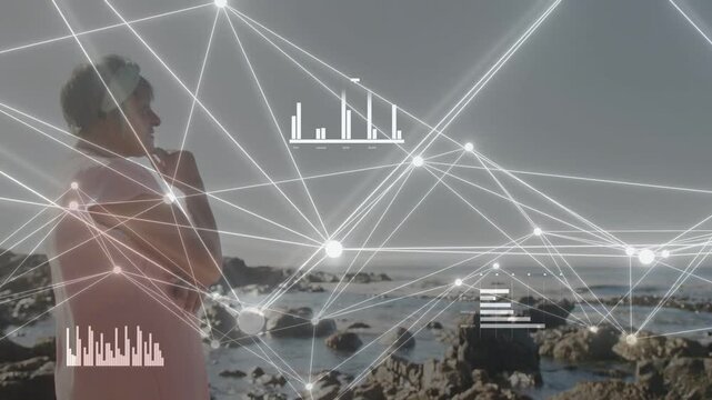 Senior woman standing on rocky coast, tech feed activating network and showing data with bar charts