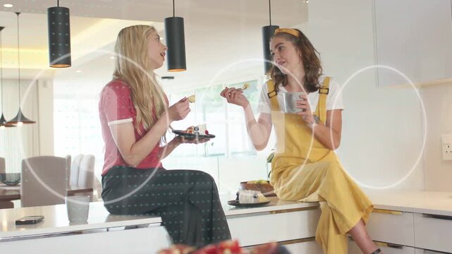 Two women on white counter right woman offering cake bite sharing treat while food overlaying faces