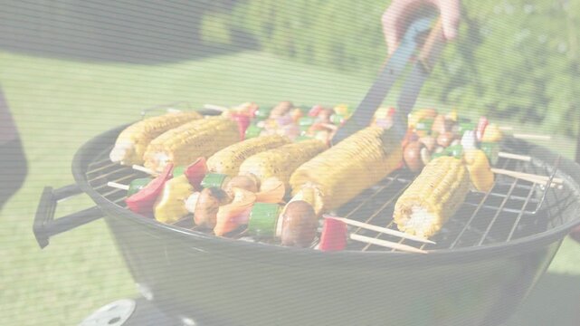 Man using tongs turning corn and skewers on charcoal grill, prompted by browning for even cooking