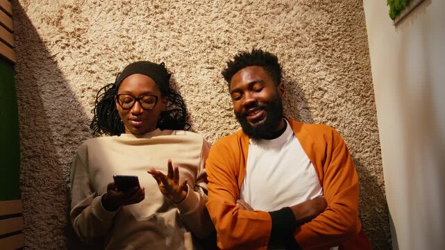 Top down view of black man and woman laughing together on hallway floor, cozy moment of laughter and romance under daylight. Couple bonding and spending quality time, positive relationship.