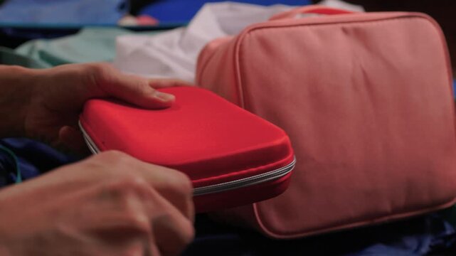 Hands opening pouch. Unzipping red case with care. Person arranging gadgets in soft fabric pouch. Close view of hands organizing electronic accessories in pouch