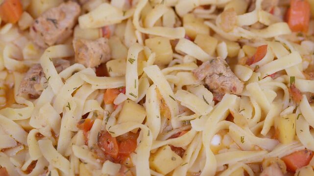 Stewed meat with noodles. Closeup of savory stewed meat and vegetables. Warm rustic setting showcasing flavorful noodles with chunks of beef and vegetables in broth