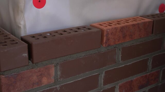Bricklaying with precision. Builder aligning bricks carefully on wall surface. Detailed view of bricklayer securing brown bricks with precision and proper tools