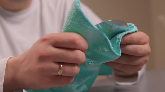 Caucasian hands polish DVD disk. Closeup of hands cleaning shiny disc carefully. Precise circular motion by hands on glossy disc with microfiber cloth in domestic setting