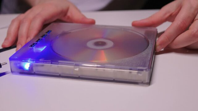 Close examination of fingers setting up DVD player with spinning disc. Focused shot of hands configuring compact DVD device with illuminated light and rotating disc