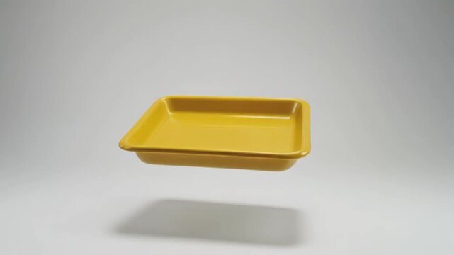 Levitating yellow rectangular plastic food tray isolated on clean gray background for minimalist product presentation