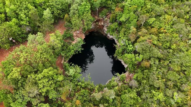 Aerial view of Sapphire Blue Hole surrounded by dense green tropical forest and limestone cliffs in The Bluff Settlement, North Eleuthera, The Bahamas.
