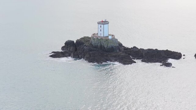Aerial view of Phare de L'Ost-Pic lighthouse standing on a dark rocky islet surrounded by the calm sea in Plouezec, Bretagne, France.