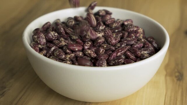 Pinto_beans_falling_into_white_bowl_on_wooden_table_4k_10bit_120fps