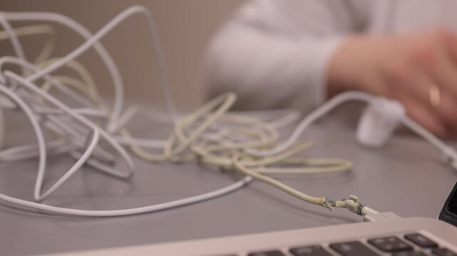 Laptop power cord repair process. Careful examination of frayed laptop connector wires. Closeup view of technician inspecting compromised power cable connections on desk