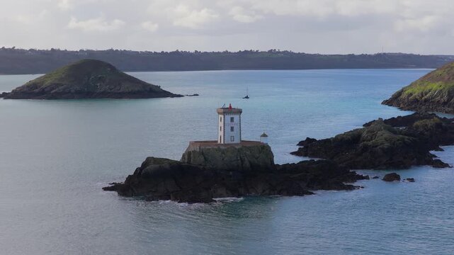 Aerial view of Phare de L'Ost-Pic lighthouse on a rocky islet surrounded by calm sea in Plouezec, Bretagne, France.