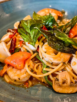 Close up, Stir-fried spicy spaghetti with mixed seafood and Thai basil, fusion cuisine  in a blue ceramic plate.