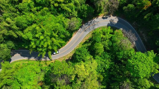 A winding road through tropical rainforest with a moving car symbolizes connected landscapes, responsible travel, forest preservation, and balance between infrastructure and nature. Thailand. 4k.
