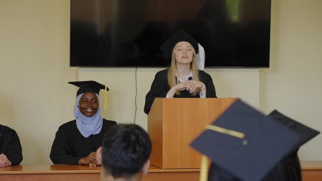 A young woman stands at the lectern and delivers a graduation speech to her classmates. 