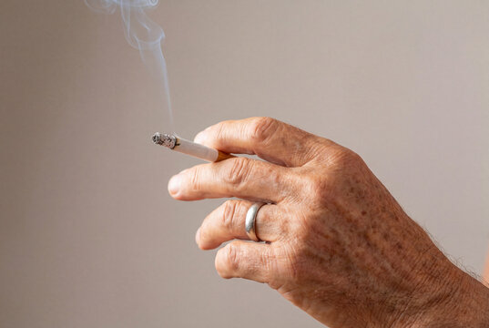 Elderly man wrinkled hand holding a lit cigarette with smoke rising