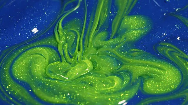 Closeup of bright green glittery slime being poured into a pool of deep blue liquid, creating dynamic splashes and swirling patterns with sparkling texture