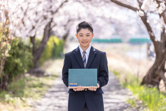 桜の前で黒板を持つ制服の男子学生
