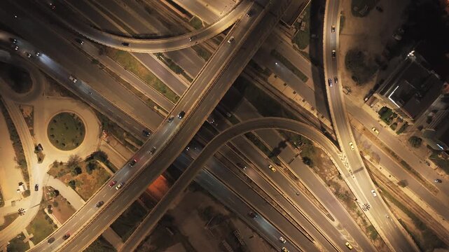 Luminous aerial view capturing the intricate network of a bustling highway interchange at night, with cars creating trails of light as they navigate the complex road system