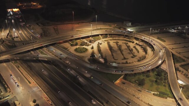 Busy urban highway interchange glowing at night, aerial view of illuminated roads, ramps and overpasses with flowing traffic showcasing modern city transportation and infrastructure