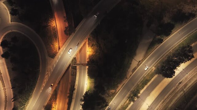Luminous aerial top-down perspective revealing a complex highway interchange with cars flowing through the illuminated road network, showcasing urban infrastructure and transportation at night