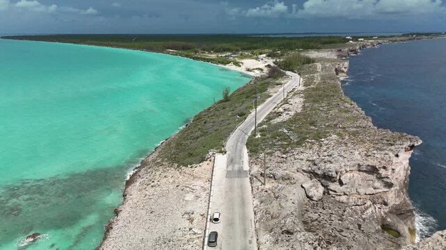 Aerial view of Glass Window Bridge separating turquoise and deep blue waters with a coastal road in Gregory Town, North Eleuthera, The Bahamas.