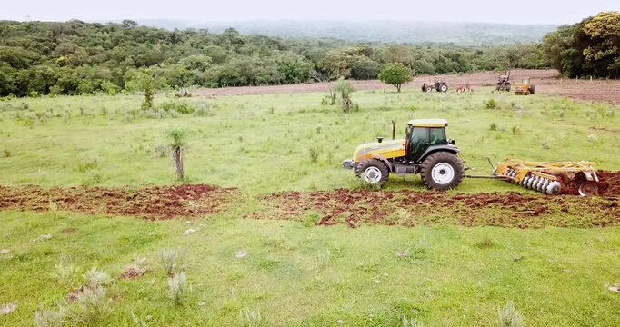 Aerial view of a modern yellow tractor with a disc harrow plowing a green field, preparing the land for planting and cultivation