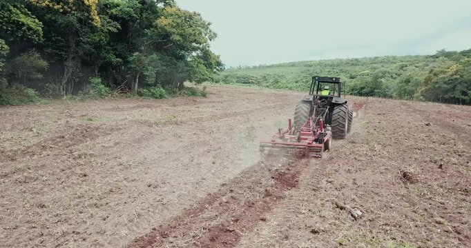Aerial view of a modern tractor plowing a dry field, preparing the land for sowing crops in the countryside with its cultivator
