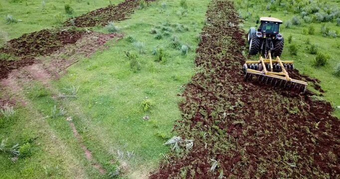 High-angle view of a tractor plowing a green field. Agricultural machinery preparing the land for planting crops in the countryside