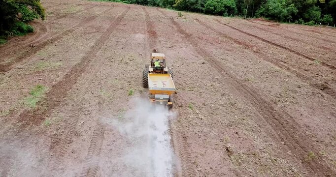 Aerial footage following a tractor as it spreads lime or fertilizer on a recently tilled field, preparing the soil for planting