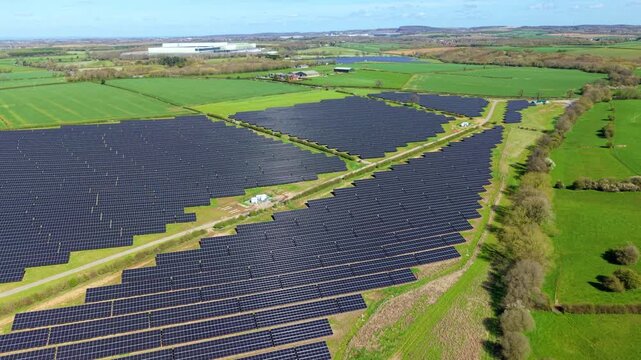 Aerial view of a large solar farm with rows of black panels surrounded by green fields and trees in Nailstone, England, United Kingdom.